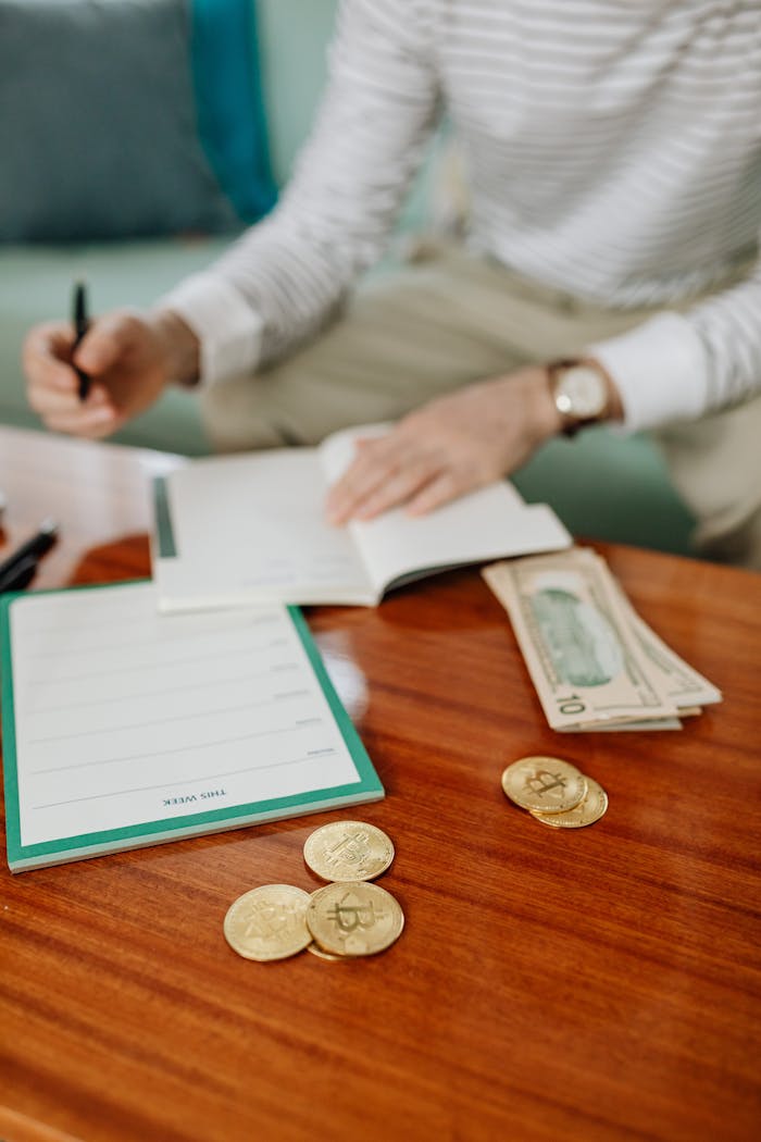 Person writing in a notebook with cash and coins on a wooden table, planning finances.